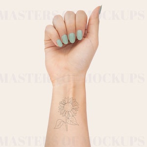 May include: A woman's wrist with a delicate line drawing tattoo of a sunflower. The tattoo is on the inside of the wrist, just below the hand. The woman is wearing light green nail polish.