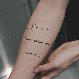 May include: A forearm with the words "Your tattoo here" written in elegant, black cursive script. The skin tone is light, and the text is centered on the arm. The image is a mockup, with the words appearing as a temporary tattoo.