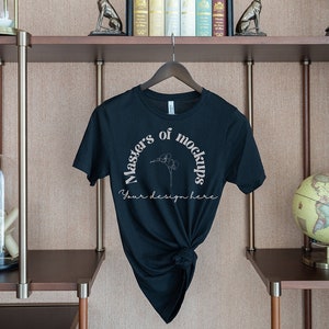May include: A black t-shirt with the text "Masters of Mockups" in a semi-circle design, with the words "Your design here" below. The shirt is hanging on a wooden hanger against a neutral background.
