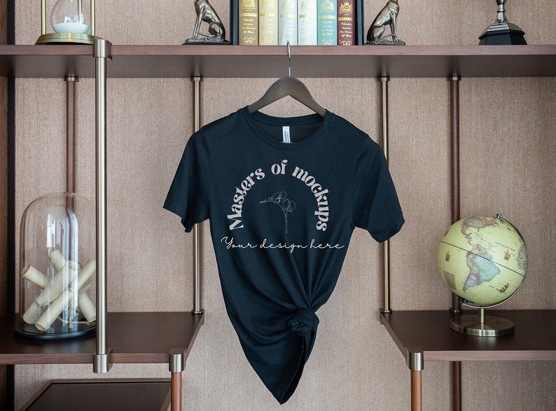 May include: A black t-shirt with the text "Masters of Mockups" in a semi-circle design, with the words "Your design here" below. The shirt is hanging on a wooden hanger against a neutral background.