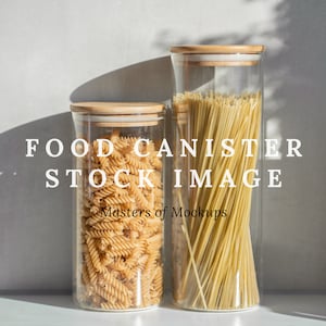Op de afbeelding: Twee glazen voedselbewaarcontainers met houten deksels. De container aan de linkerkant bevat gedroogde pastaspiralen. De container aan de rechterkant bevat lange, dunne spaghetti-noedels.