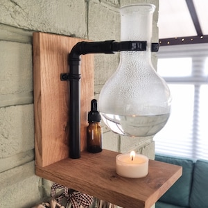 May include: A wooden shelf with a glass diffuser, a small bottle, and a candle. The diffuser is filled with water and has a small flame underneath it. The shelf is mounted on a brick wall.