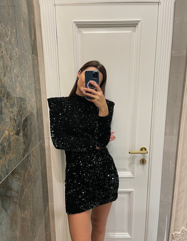 May include: A black sequined dress with long sleeves and a high neckline. The dress is a mini-skirt style, reflecting light. The garment is suitable for special occasions and evening wear.