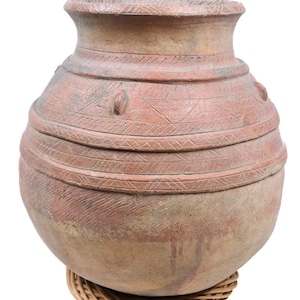 Puede incluir: Una olla grande, redonda, de terracota con una boca ancha y una base tejida. La olla está decorada con intrincados patrones y tiene un color marrón rojizo.
