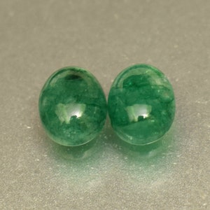 May include: Two round, green emerald gemstones. The gemstones are smooth and polished.
