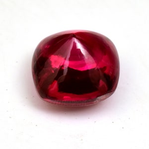 May include: A deep red gemstone with a faceted cut. The gemstone is round and has a pointed top.