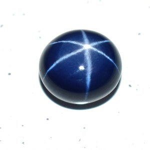 May include: A deep blue star sapphire gemstone with a six-pointed star in the center. The star is formed by the reflection of light through the stone.