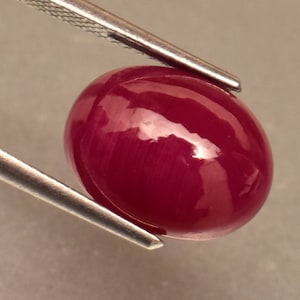 Könnte beinhalten: Ein ovaler Edelstein in tiefroter Farbe mit einer glatten, polierten Oberfläche.