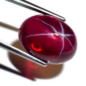 Könnte beinhalten: Ein tief roter Sternrubin-Edelstein mit einem Cabochon-Schliff und einem sternförmigen Muster.
