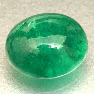 Pode incluir: Uma gema de esmeralda verde vibrante, cortada em forma oval. A pedra &eacute; lisa e polida, com um leve brilho.