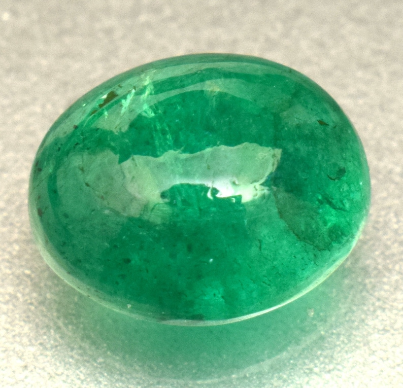 Pode incluir: Uma gema de esmeralda verde vibrante, cortada em forma oval. A pedra &eacute; lisa e polida, com um leve brilho.