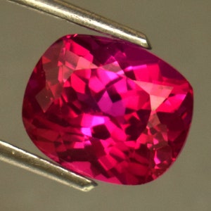 Op de afbeelding: Een levendige roze edelsteen met een kussen-slijpvorm. De edelsteen is gefacetteerd en heeft een hoge glans.