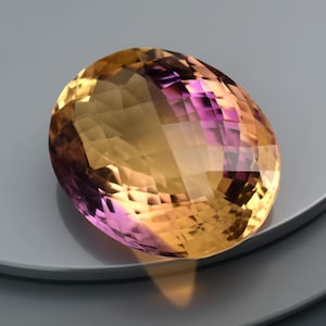 May include: An oval-shaped gemstone with a mix of yellow, orange, and purple hues. The gem is cut with multiple facets, creating a sparkling effect. The gemstone is set against a neutral background.