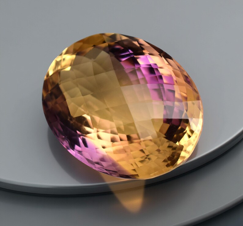 May include: An oval-shaped gemstone with a mix of yellow, orange, and purple hues. The gem is cut with multiple facets, creating a sparkling effect. The gemstone is set against a neutral background.