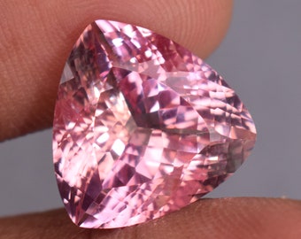 May include: A pink gemstone with a triangular cut and a faceted surface.