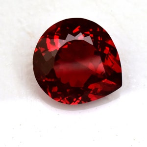 Puede incluir: Una piedra preciosa de color rojo intenso en forma de pera con facetas.