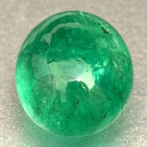 Pode incluir: Uma gema de esmeralda redonda, verde brilhante, com uma superf&iacute;cie lisa e polida.