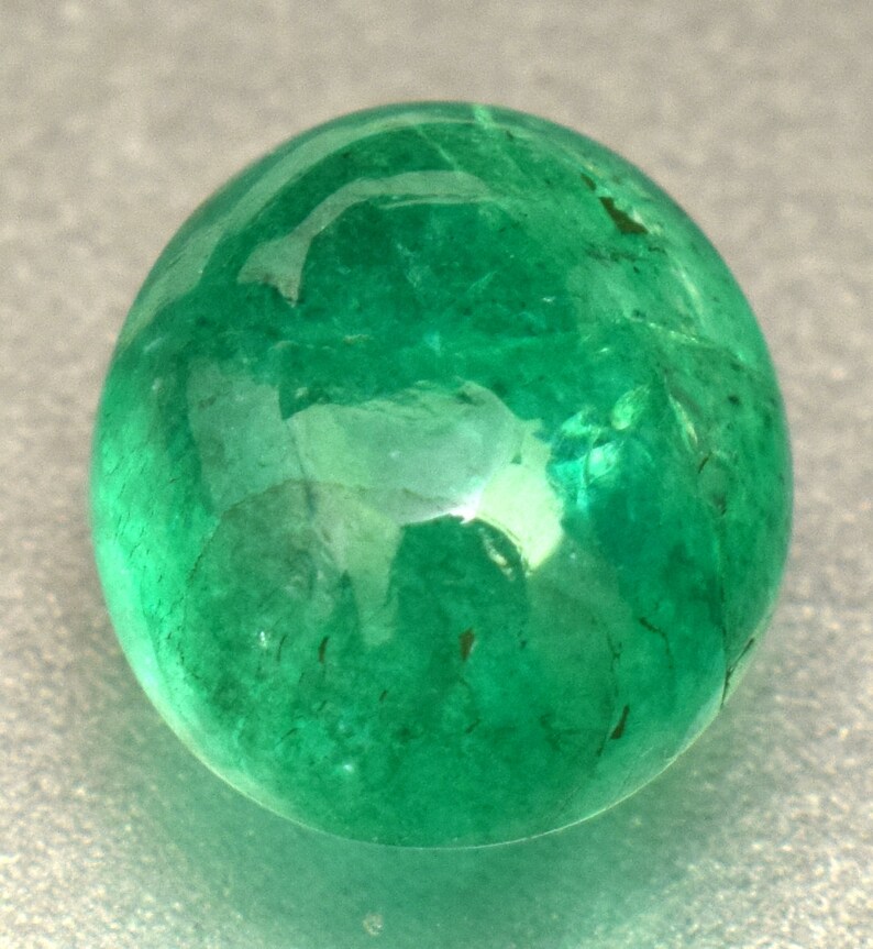Pode incluir: Uma gema de esmeralda redonda, verde brilhante, com uma superf&iacute;cie lisa e polida.