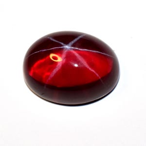 May include: A red star ruby gemstone with a star-like pattern in the centre.