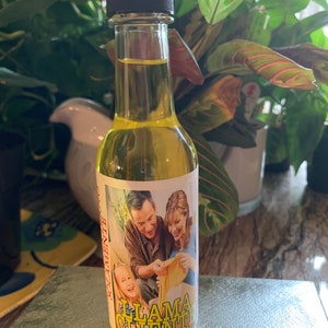 May include: A small glass bottle with a yellow liquid inside. The bottle has a label with a picture of a family and the text "Llama Cliente".