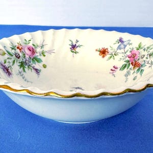May include: A white porcelain bowl with a scalloped rim and gold trim. The bowl is decorated with floral patterns in pink, purple, and orange. The bowl is a decorative piece.