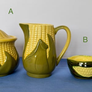 Könnte beinhalten: Ein Küchenset aus Keramik mit Mais-Motiv, bestehend aus einer Zuckerdose mit Deckel, einem Krug und einer kleinen Schüssel mit Griff. Das Set ist in Gelb- und Grüntönen gehalten und hat ein strukturiertes Maiskolben-Design.