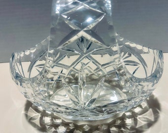May include: A clear crystal basket with a cut glass design. The basket has a handle and is perfect for holding small items.