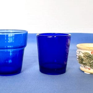 May include: Two cobalt blue glass vessels and one small ceramic planter. The first glass vessel has a flared rim, the second is a straight-sided cylinder, and the ceramic planter features a painted green ivy leaf pattern with small red berries.