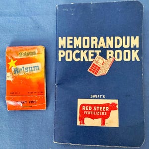 May include: An orange and yellow bobby pin box with the text "Helsum" and a blue memorandum pocket book with the text "Memorandum Pocket Book" and "Swift's Red Steer Fertilizers".