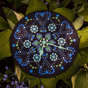 May include: A black clock with a mandala design painted in blue, green, and white dots. The clock hands are green.