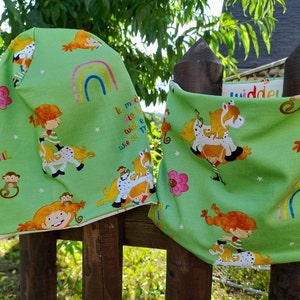 Könnte beinhalten: Zwei grüne Stoff-Stirnbänder mit weißem Rand. Beide Stirnbänder zeigen einen bunten Regenbogen, Sterne und ein sich wiederholendes Muster von Kindern, die auf Pferden reiten. Der Text "It makes me smile" ist auf einem Stirnband gedruckt.