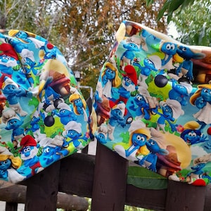 Könnte beinhalten: Zwei blaue und weiße Stoffquadrate mit einem Muster von Schlumpf-Charakteren. Der Stoff ist aus einer weichen Baumwollmischung gefertigt und perfekt für Bastelarbeiten.