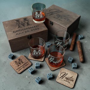 May include: A wooden gift set with two engraved boxes, two whiskey glasses, coasters, and ice cubes. The glasses and coasters have custom text. The set includes cigars and whiskey stones.