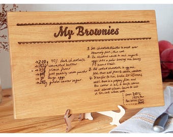Könnte beinhalten: Ein Holzbrett zum Schneiden mit einem eingravierten Rezept für Brownies. Das Rezept enthält Zutaten wie dunkle Schokolade, ungesalzene Butter, Mehl, Kakaopulver, Eier und braunen Zucker. Das Rezept enthält auch Anweisungen zum Backen der Brownies bei 200 °C für 23 Minuten.