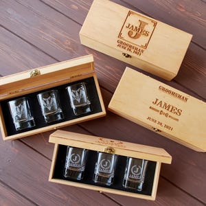 May include: Three wooden boxes with engraved text, each containing three shot glasses. The boxes are labeled "Groomsmans" with the name "James" and the date "June 20, 2021".
