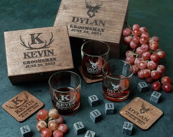 May include: A set of personalized wooden boxes and glasses for a groomsman. The boxes are engraved with the names "Kevin" and "Dylan" and the date "June 20, 2023". The glasses are engraved with a deer head and the names "Kevin" and "Dylan".