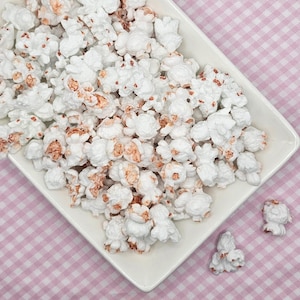 Op de afbeelding: Een wit keramiek bord gevuld met witte popcorn met een licht roze tint. De popcorn is willekeurig op het bord gerangschikt.