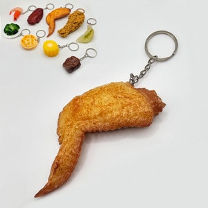 May include: A fried chicken wing keychain with a gold chain. The chicken wing is a realistic replica of a fried chicken wing.