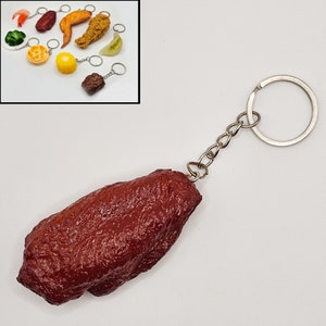 May include: A red, brown, and silver keychain with a realistic-looking chicken wing charm. The keychain is made of metal and has a silver ring for attaching to keys.