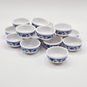 May include: A stack of white ceramic bowls with a blue and green floral design. The bowls are stacked in a pyramid shape.