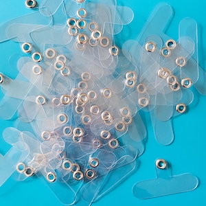 May include: A pile of clear plastic badge holders with silver metal eyelets. The holders are arranged in a random pattern on a bright blue background.