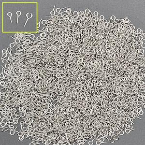 May include: A large quantity of silver-toned eyelet screws, also known as screw-back findings, are piled together. The eyelet screws have a small loop at the top and a screw post at the bottom.