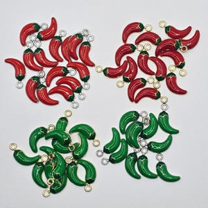Könnte beinhalten: Eine Sammlung roter und grüner Chili-Pfeffer-Anhänger. Die roten Paprika haben grüne Stiele und goldfarbene Schlaufen. Die grünen Paprika haben goldfarbene Schlaufen. Diese Anhänger sind ideal für die Schmuckherstellung oder andere Bastelprojekte.