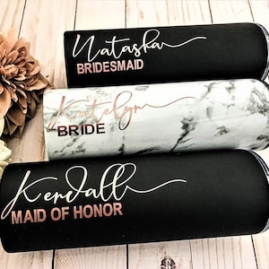 May include: Three black and white stainless steel tumblers with rose gold lettering. The tumblers are personalised with the names Natasha, Katelyn, and Kendall. The text on the tumblers reads "Bridesmaid", "Bride", and "Maid of Honour".