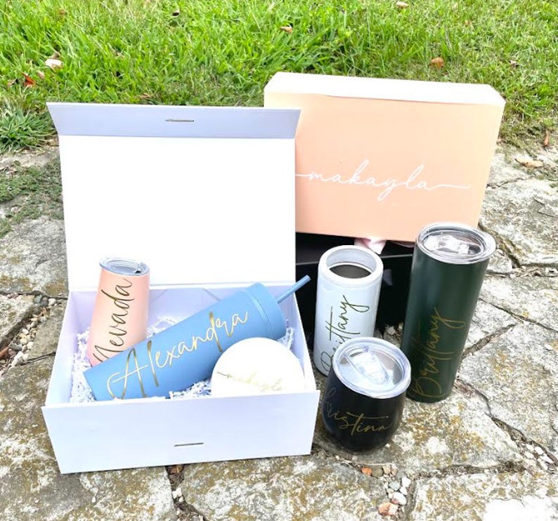 May include: A set of five personalised tumblers in a white gift box. The tumblers are in various colours, including blue, pink, green, and black. Each tumbler has a gold name on it: "Alexandra", "Brittany", "Makayla", "Nevada", and "Christina".