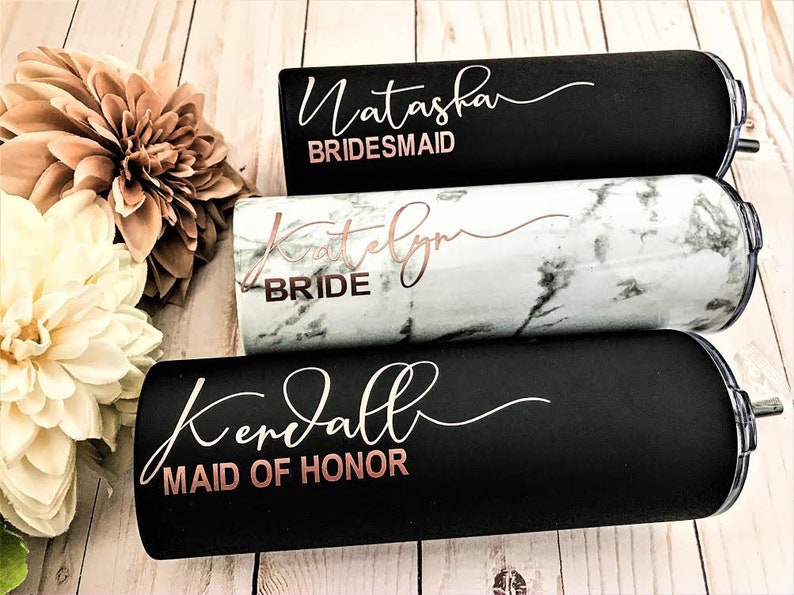 May include: Three black and white stainless steel tumblers with rose gold lettering. The tumblers are personalised with the names Natasha, Katelyn, and Kendall. The text on the tumblers reads "Bridesmaid", "Bride", and "Maid of Honour".