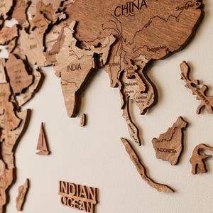 Pode incluir: Um mapa-m&uacute;ndi de madeira com pe&ccedil;as individuais de pa&iacute;ses, incluindo &Iacute;ndia, China e Indon&eacute;sia. O mapa &eacute; feito de madeira castanha clara e est&aacute; montado numa parede de cor neutra. As palavras "Oceano &Iacute;ndico" tamb&eacute;m s&atilde;o vis&iacute;veis.