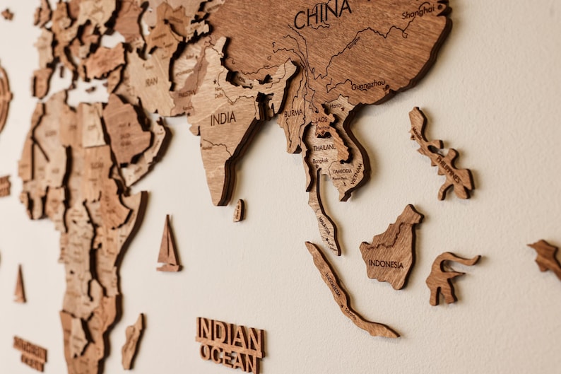 Pode incluir: Um mapa-m&uacute;ndi de madeira com pe&ccedil;as individuais de pa&iacute;ses, incluindo &Iacute;ndia, China e Indon&eacute;sia. O mapa &eacute; feito de madeira castanha clara e est&aacute; montado numa parede de cor neutra. As palavras "Oceano &Iacute;ndico" tamb&eacute;m s&atilde;o vis&iacute;veis.