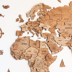 Pode incluir: Um mapa-m&uacute;ndi de madeira com pe&ccedil;as de pa&iacute;ses individuais, incluindo o texto "Arctic Ocean" e "Southern Ocean". O mapa apresenta contornos detalhados dos pa&iacute;ses e &eacute; acompanhado por recortes de madeira de avi&otilde;es e barcos.