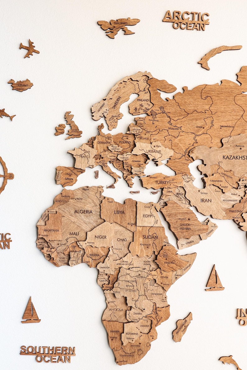 Pode incluir: Um mapa-m&uacute;ndi de madeira com pe&ccedil;as de pa&iacute;ses individuais, incluindo o texto "Arctic Ocean" e "Southern Ocean". O mapa apresenta contornos detalhados dos pa&iacute;ses e &eacute; acompanhado por recortes de madeira de avi&otilde;es e barcos.